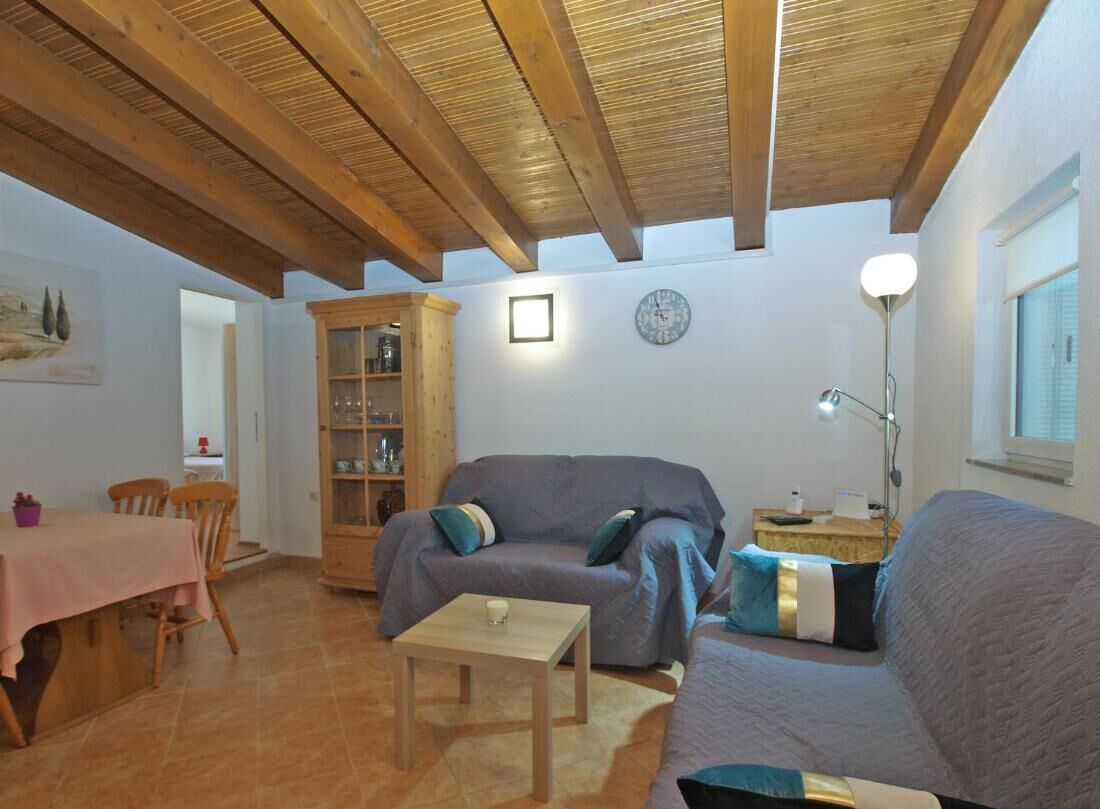 Una sala de estar acogedora con techo de madera, un sofá gris, un aparador de madera y una mesa de comedor con sillas.