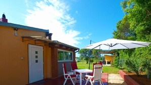 Un patio con una mesa, sillas, una sombrilla blanca y una puerta a un edificio.