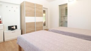 Un dormitorio con dos camas, un armario, un televisor y un baño visible a través de una puerta abierta.