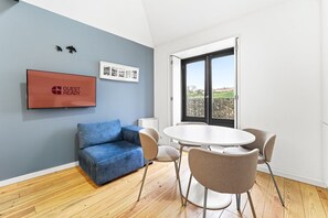 Una habitación con un sofá azul, una mesa redonda con sillas, un televisor en la pared y un ventanal con vistas.