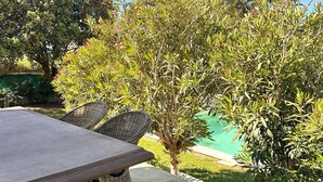 A patio area with a table and wicker chairs, surrounded by lush greenery and a pool. - Les Lauriers Roses house with swimming pool - popular area Isle sur la Sorgue (L'Isle-sur-la-Sorgue)