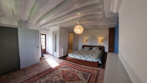 Een slaapkamer met een bed, twee bedlampen, een kamerkleed met een patroon, en een plafond met zichtbare balken.