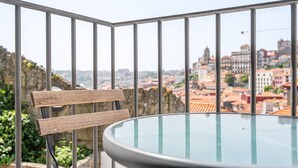 A balcony with a glass table and a wooden bench, overlooking a cityscape with historic buildings. - GuestReady - Old City Design - Faces (Porto)