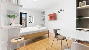 A modern hotel room with a bed, a desk, a chair, a TV, and a city view. - GuestReady - Old City Design - Faces (Porto)