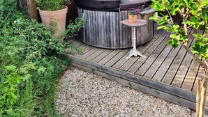 A wooden deck with a hot tub, a potted plant, and a small table with a flower pot. - Studio Mandavi - Vineyards & Forest (Loupes)