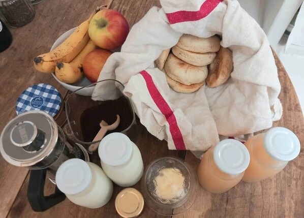 A wooden table with a bowl of apples and bananas, a cloth bag with bread, and several bottles of liquids.