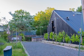 A rustic barn with a sloped roof, a gravel driveway, and a vineyard in the foreground.