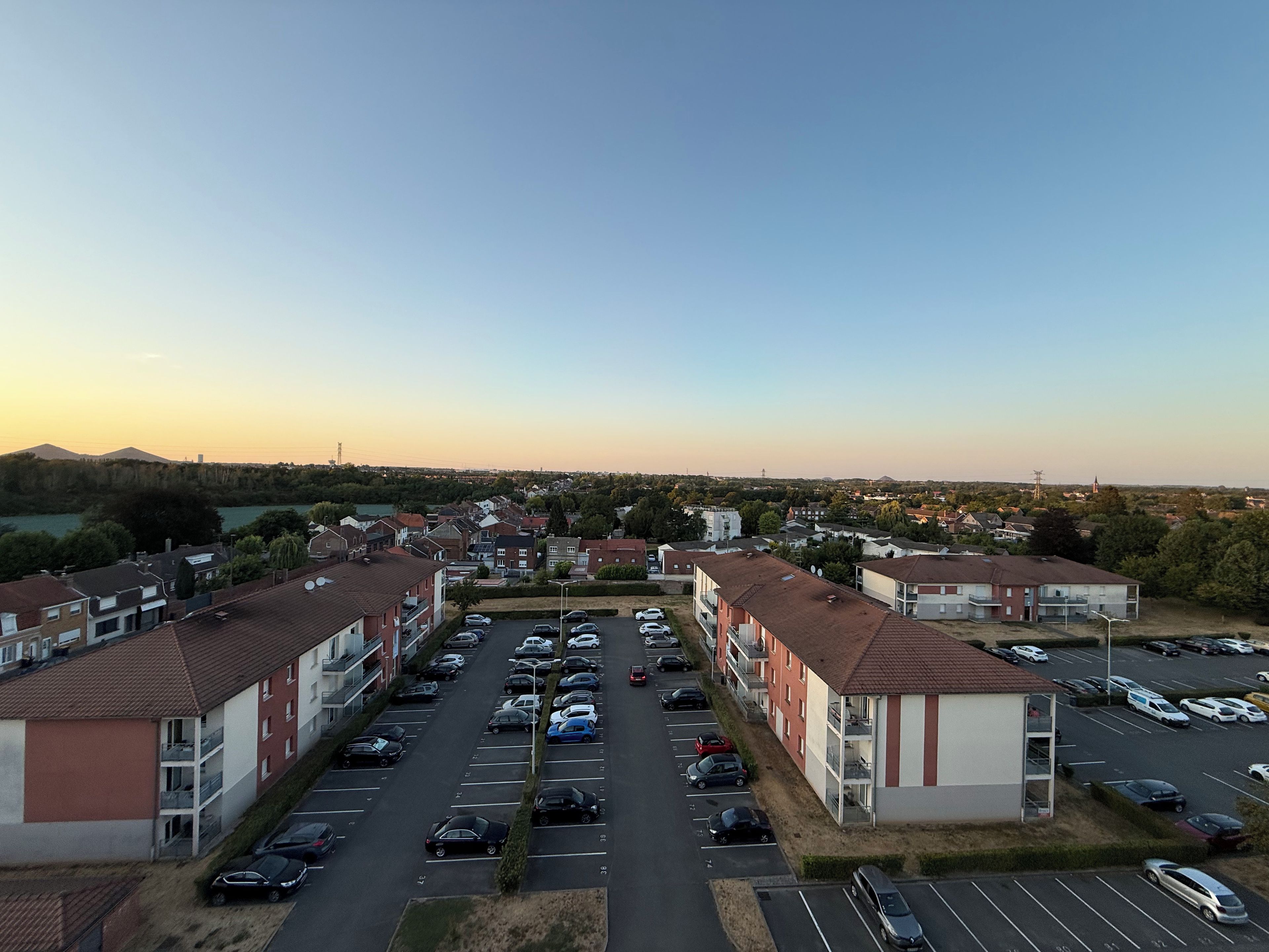 Un parking à étages où les voitures sont garées en rangées, entouré d’immeubles aux façades rouges et blanches.