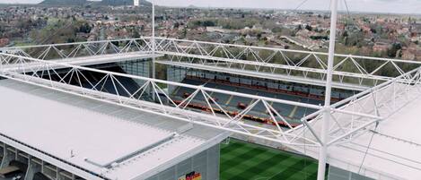 A stadium with a white roof and a green field, surrounded by a cityscape and mountains.