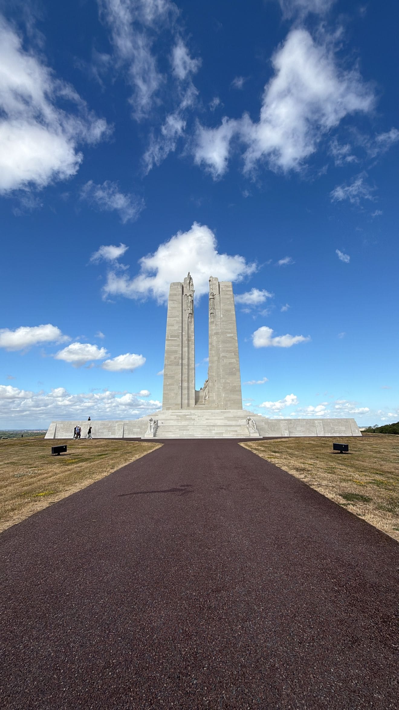 Un monumento con una estatua central, flanqueado por dos altos pilares, situado en un extenso campo abierto con cielo despejado.