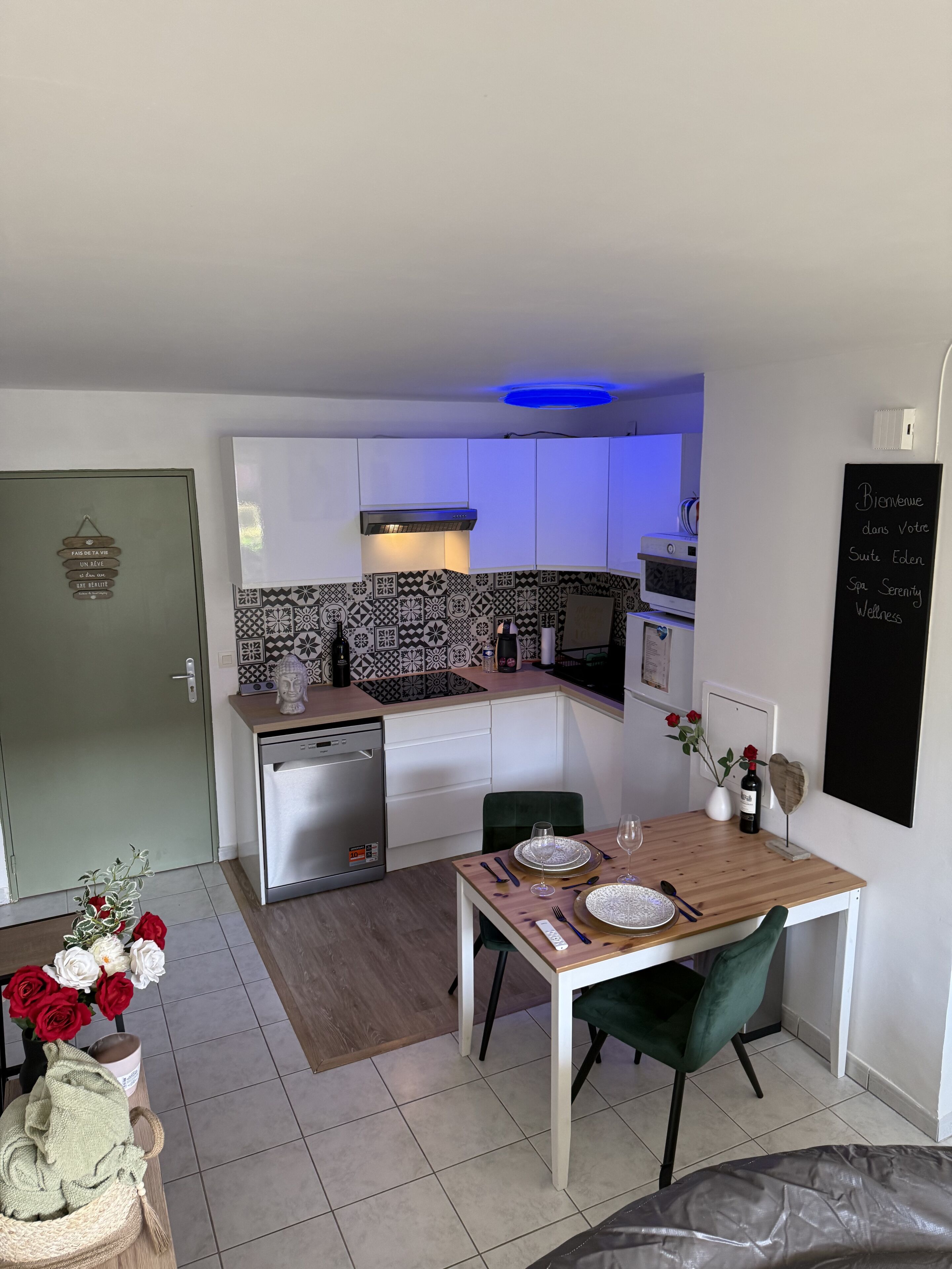 Una cocina compacta con armarios blancos, salpicadero blanco y negro, e iluminación azul en el techo.