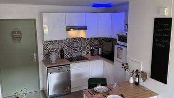 Une cuisine de taille réduite avec des meubles blancs, un pare-feu noir et blanc et un plafond éclairé de lumière bleue.