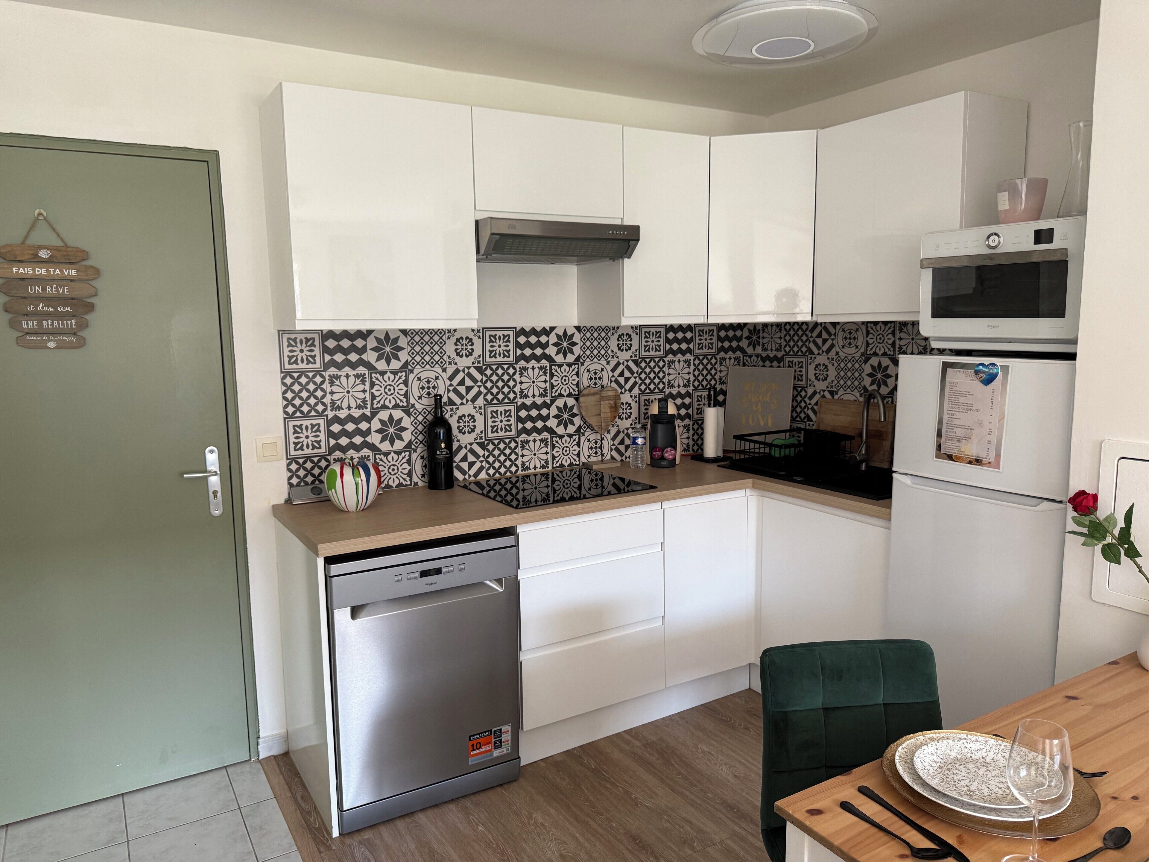 A compact kitchen with white cabinets, a stainless steel dishwasher, a microwave, and a patterned backsplash.