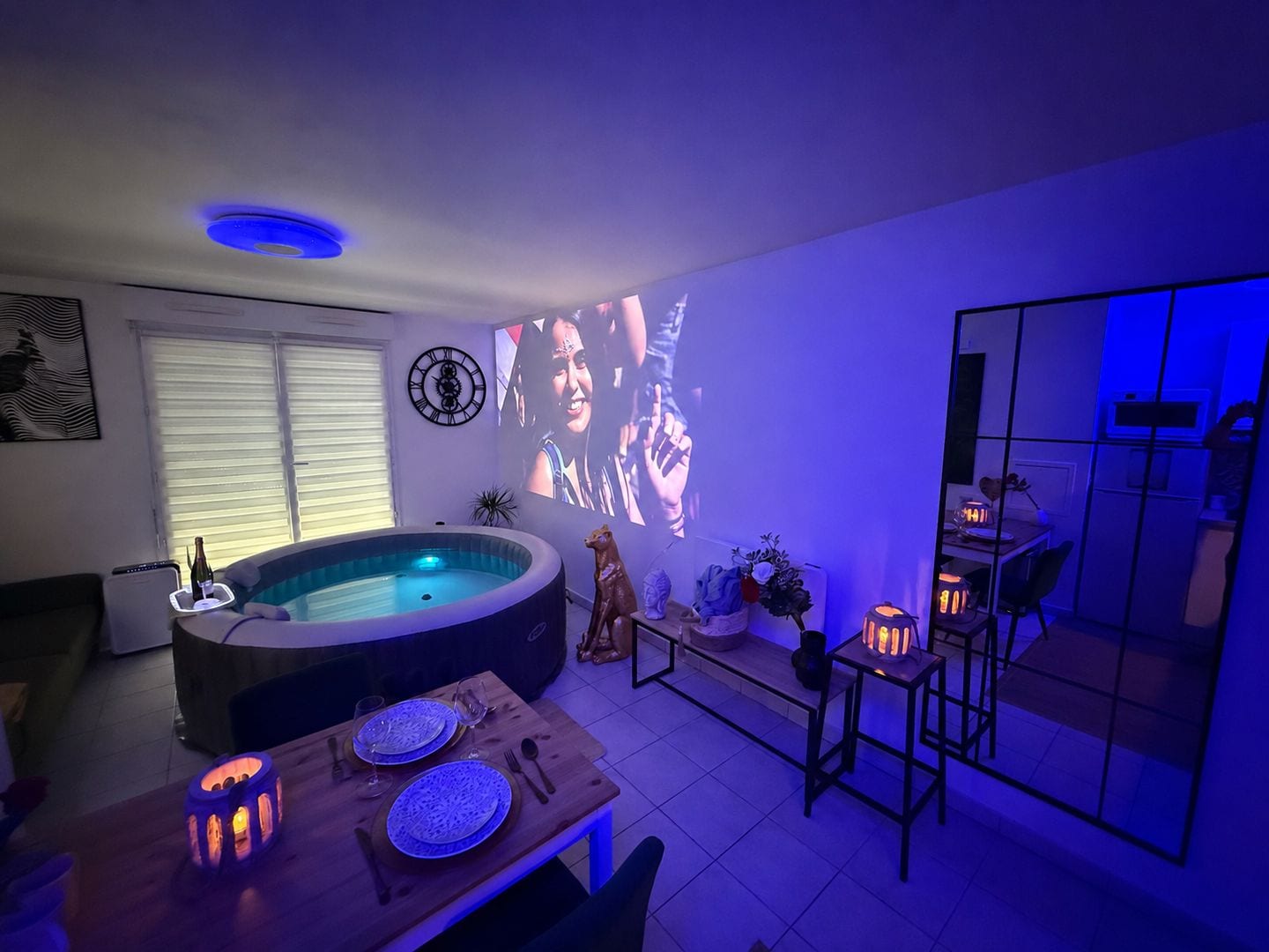 A living room with a hot tub, a dining table set for two, and a projection screen displaying a movie.