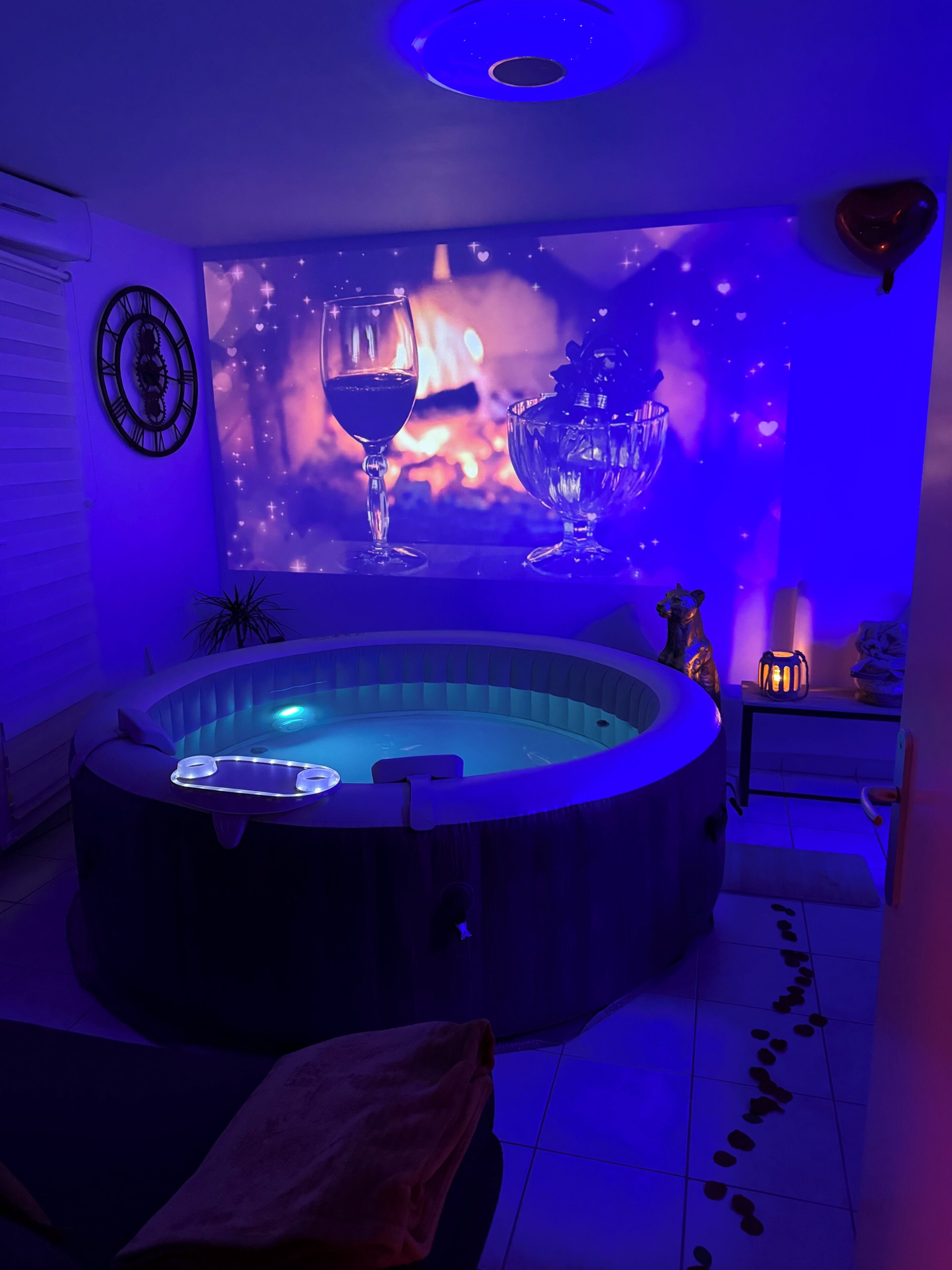 Un bain à remous dont le mur est décoré d’une projection représentant un verre de vin et des flammes, ainsi qu’une horloge et une petite table sur laquelle est posée une bougie.