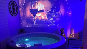 Un bain à remous dont le mur est décoré d’une projection représentant un verre de vin et des flammes, ainsi qu’une horloge et une petite table sur laquelle est posée une bougie.