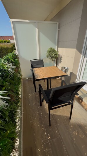 Un patio al aire libre con una mesa de madera y sillas negras, una planta pequeña en maceta y un cubo de metal.