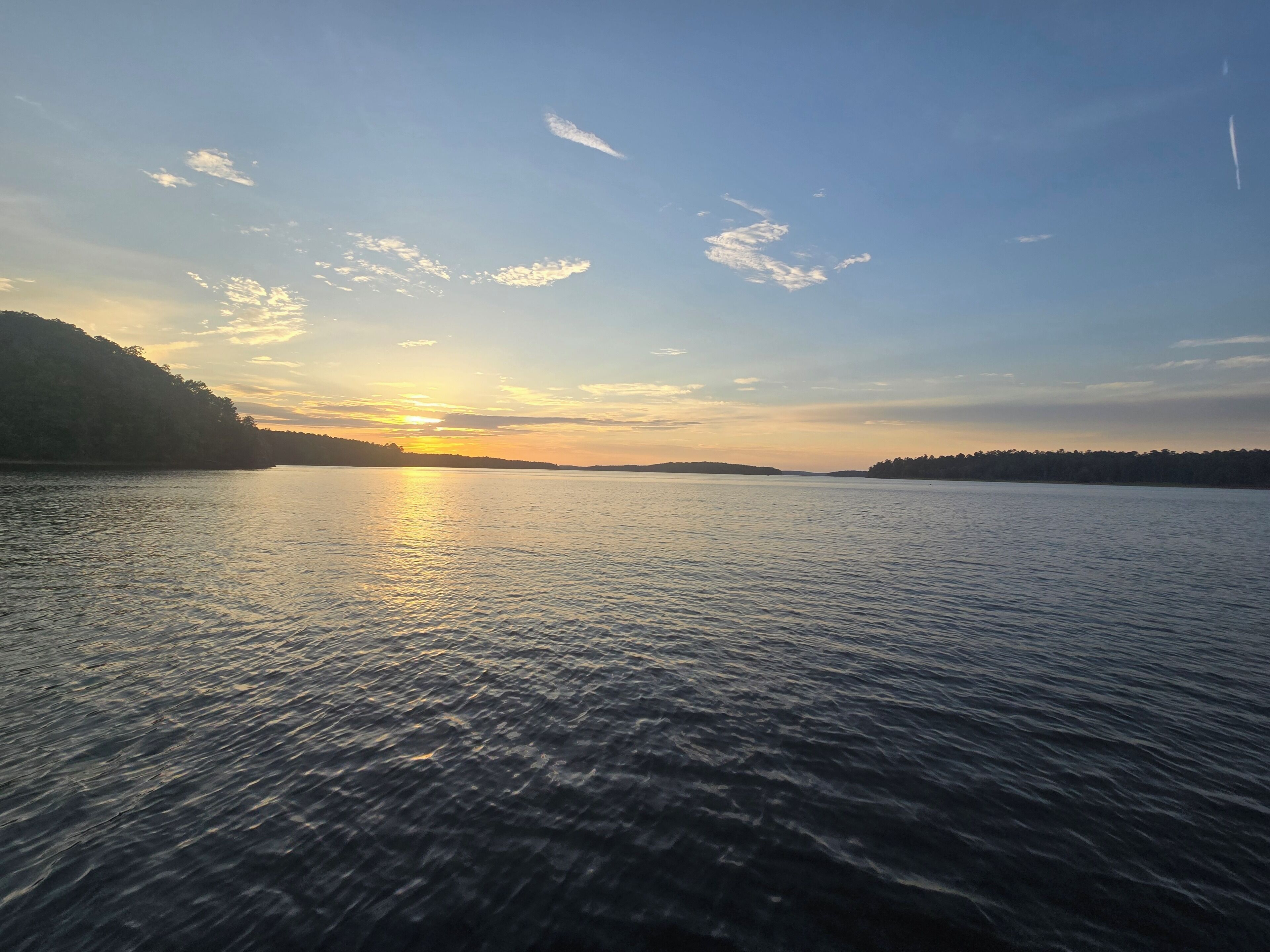 A calm body of water with a sunset in the background and hills on either side.