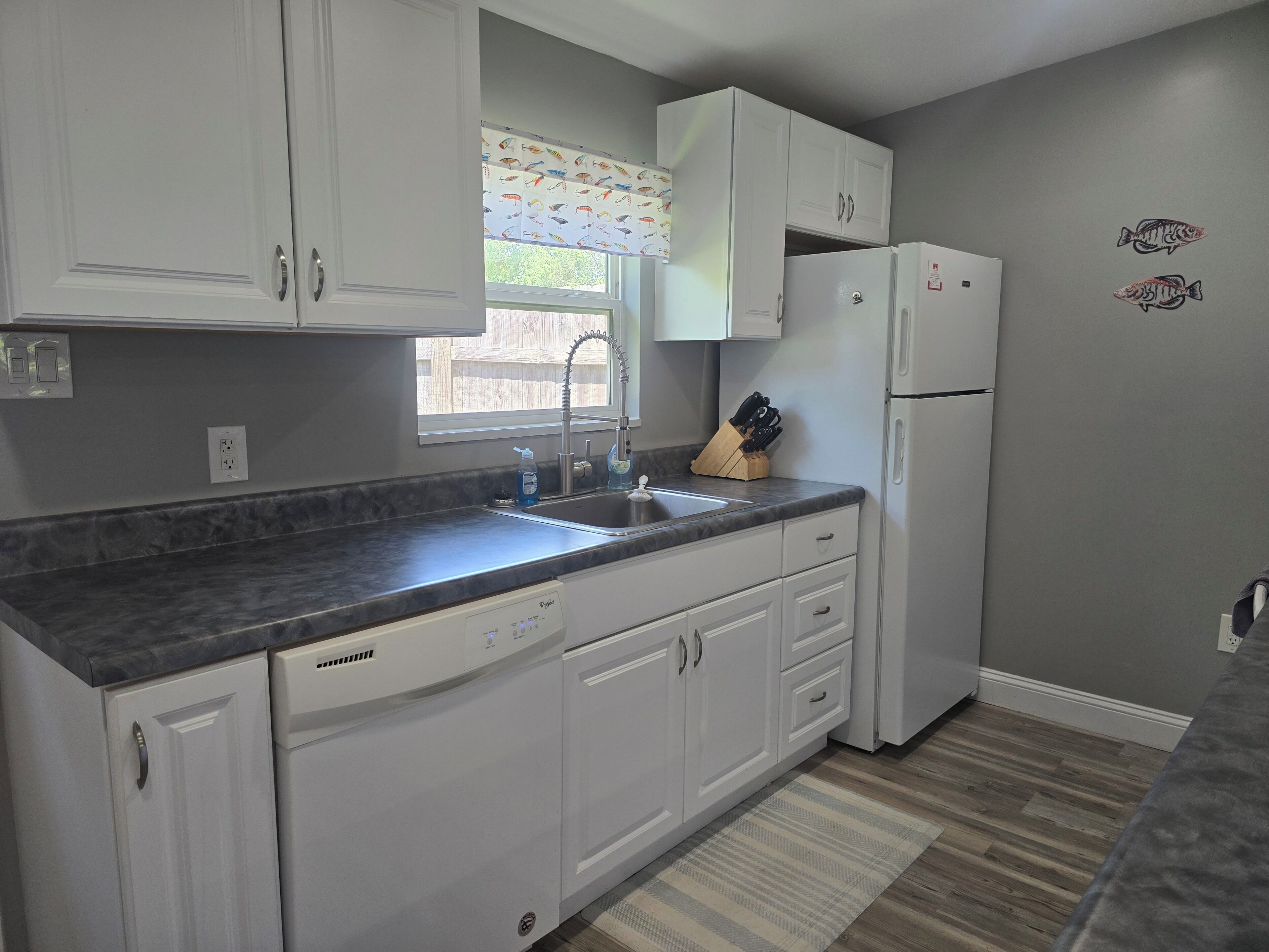 A kitchen with white cabinets, a dishwasher, a refrigerator, and a window with a view of the outside.