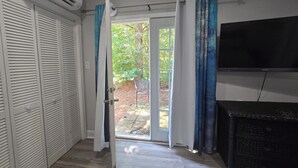 A room with a sliding glass door leading to a garden, a white closet with louvered doors, and a flat-screen TV mounted on the wall.