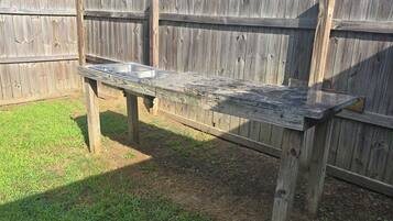 A wooden picnic table with metal containers, set against a wooden fence in a grassy area.