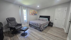 A bedroom with a bed, a chair, a nightstand, and a door.