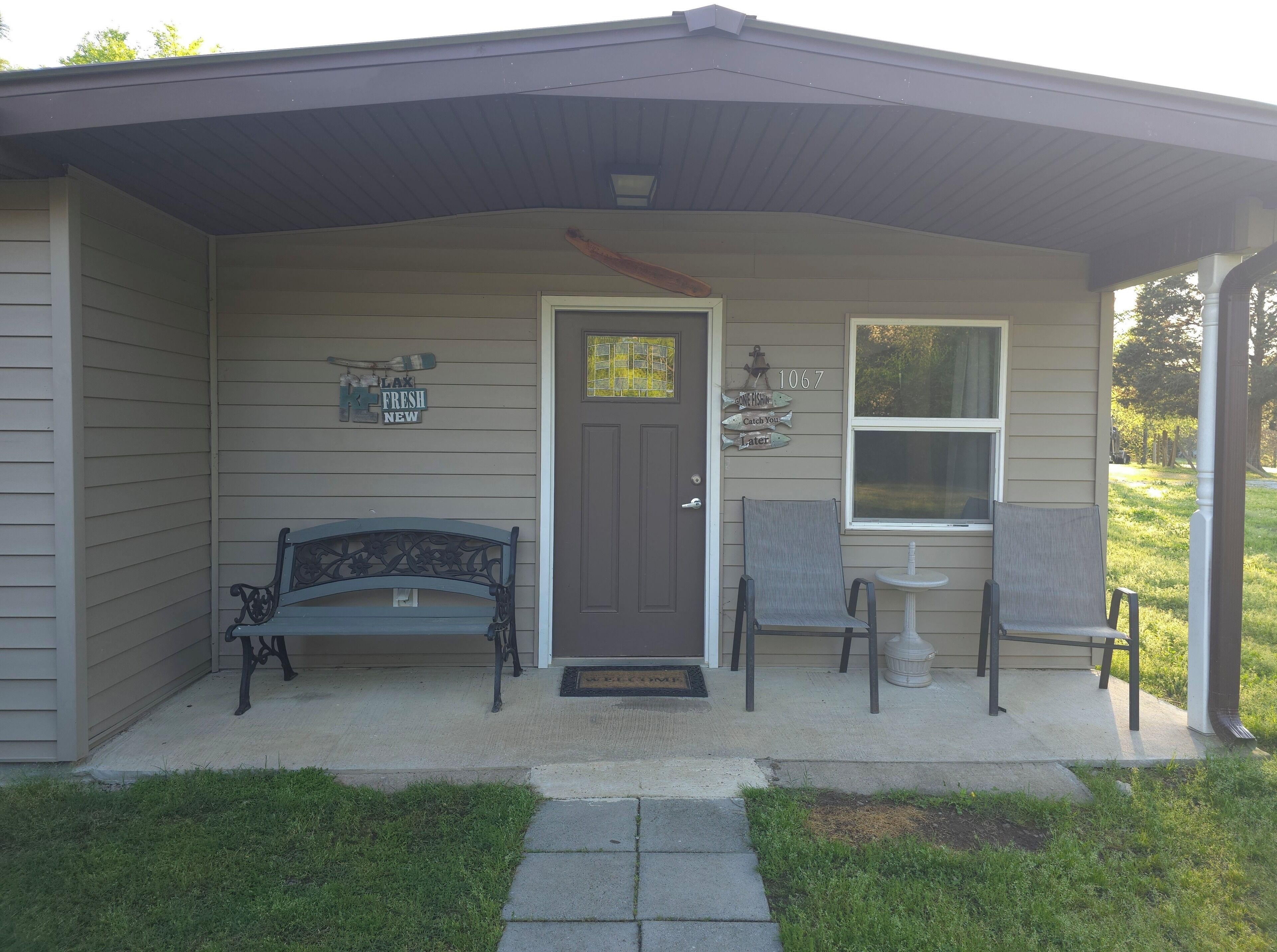 A house with a porch, a bench, two chairs, a small table, and a door with a number sign.