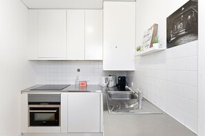 A modern kitchen with white cabinets, a black induction cooktop, a built-in oven, a stainless steel sink, and a coffee maker.