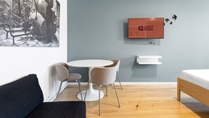 A modern room with a round table, two chairs, a bed, a mounted TV, and a wall-mounted shelf.
