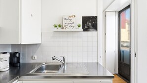 A modern kitchen with white cabinets, a stainless steel sink, a coffee maker, and a framed inspirational quote on the wall.