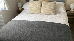 A neatly made bed with a dark quilt and patterned pillows, a wooden headboard, and bedside lamps on wooden nightstands.