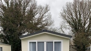 A small, single-story mobile home with a white exterior, a covered porch with white railings, and a number '3' sign on the right side.