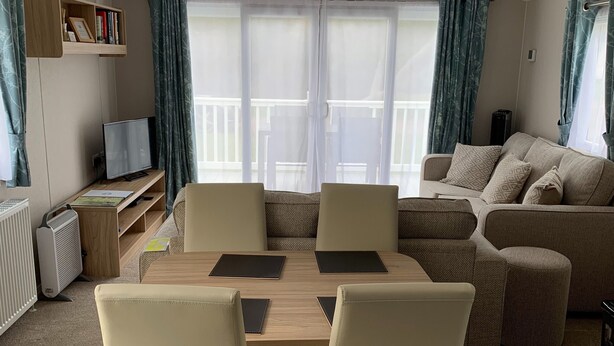 A modern living room with a wooden dining table, four chairs, a sofa, and a TV on a shelf.