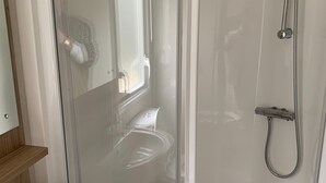 A modern bathroom with a glass-enclosed shower, a white sink, and a wooden shelf.