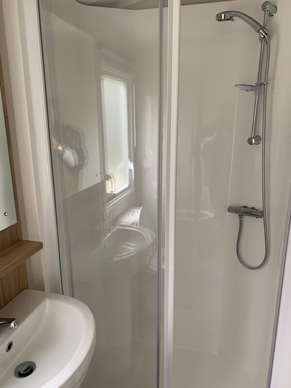 A modern bathroom with a glass-enclosed shower, a white sink, and a wooden shelf.
