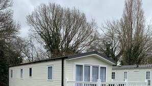 A mobile home with a covered porch and a fenced deck area.