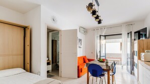 Ein modernes Hotelzimmer mit Bett, einem Essbereich mit Tisch und Stühlen sowie einer Küchenzeile mit einer Mikrowelle.