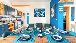 Una cocina moderna con armarios azules, una zona de comedor con mesa de madera preparada para una comida, y una pared de acento en tono azul.