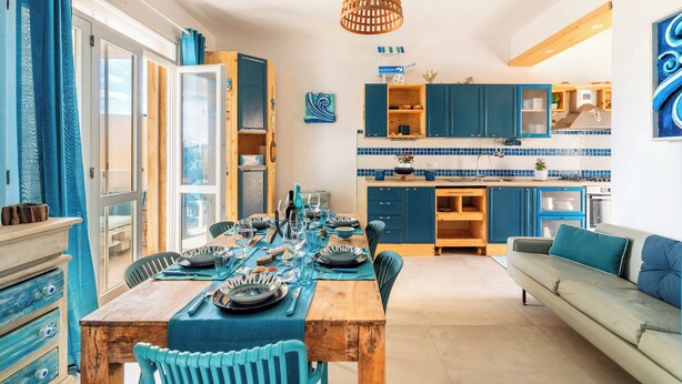Una cocina moderna con armarios azules y un comedor con una mesa de madera dispuesta para una comida.