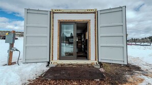 A small, enclosed structure with a sliding door, a wooden frame, and a metal exterior. - Farm Stay, 1-bedroom custom built shipping container on the river. (Ovando)