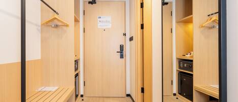 A hallway with wooden walls, a bench, a door with a calendar, and a small kitchen area with a microwave and refrigerator.