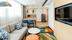 Een moderne hotelkamer met een bank, stoelen, een kleine tafel, een televisie en een keuken in de achtergrond.