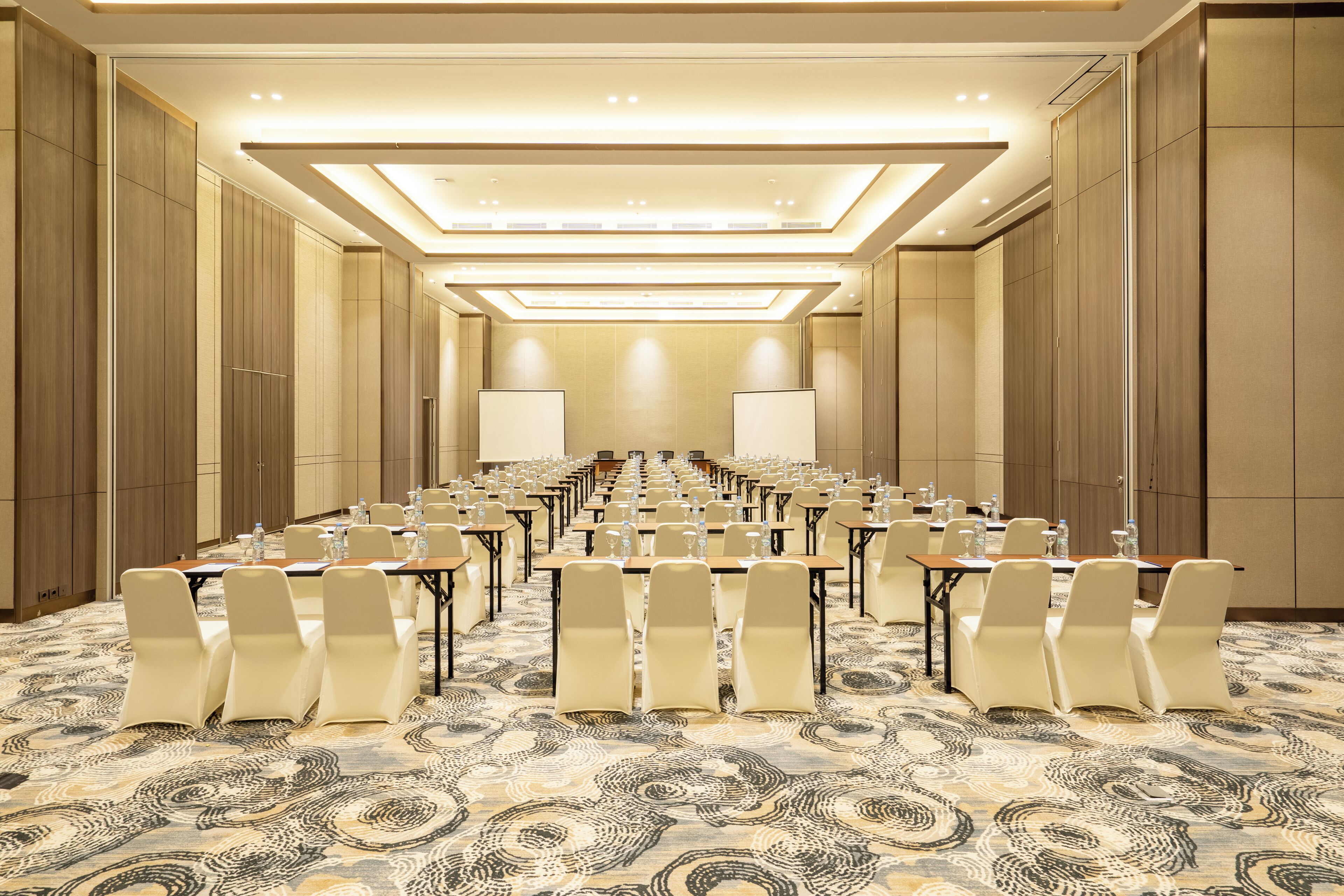 Une salle de conférence dotée de plusieurs tables et chaises, d’un tapis à motifs et d’un plafond au design moderne.