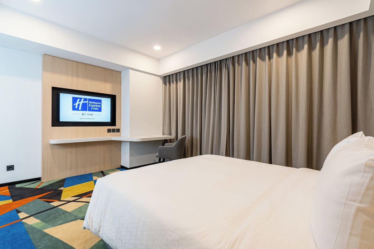 Een hotelkamer met een bed, een aan de muur bevestigde televisie, een bureau en een stoel.