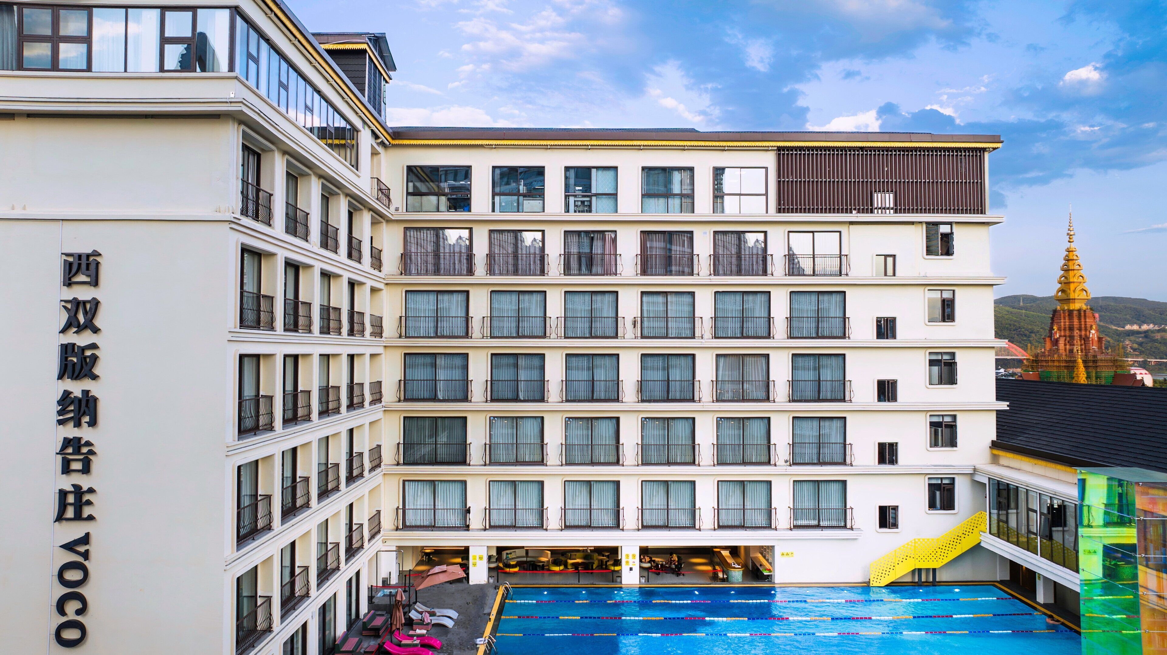 Un hotel de varios pisos con piscina, balcones y una gran estatua de Buda al fondo.