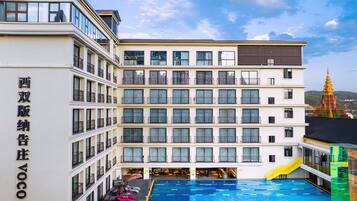 Un hotel de varios pisos con piscina, balcones y una gran estatua de Buda al fondo.