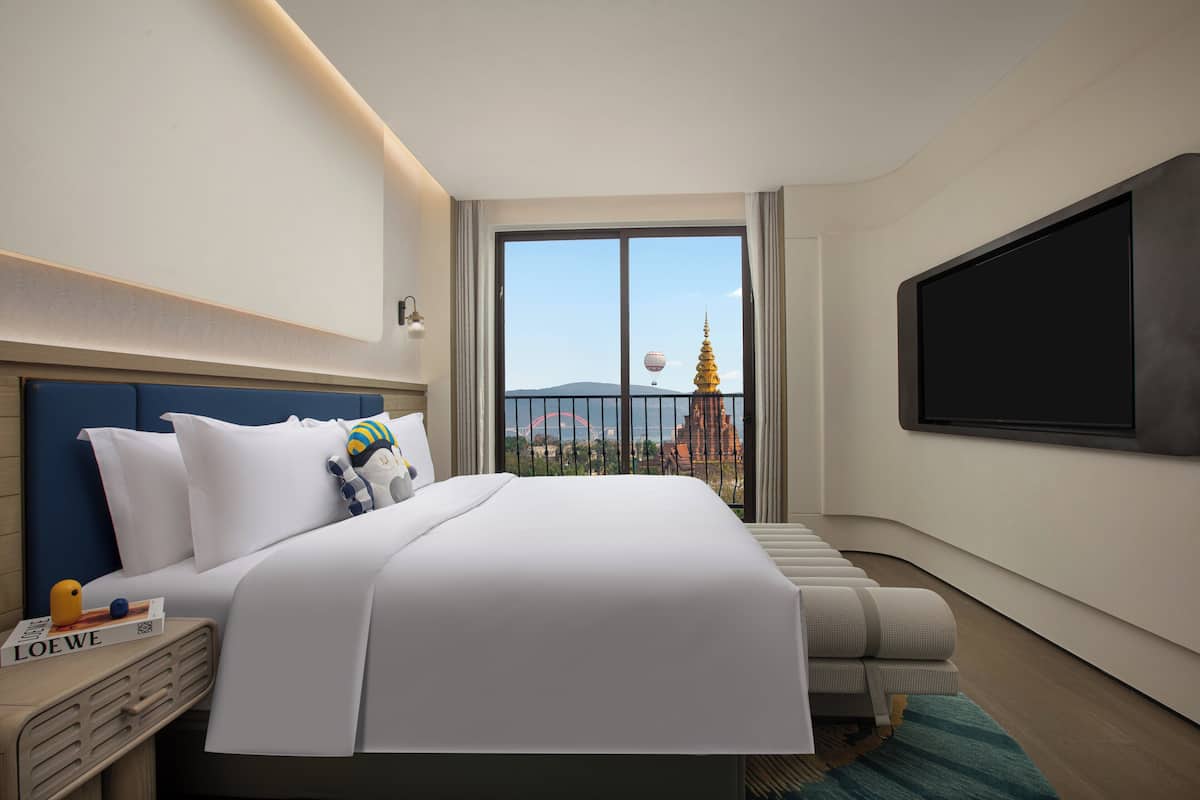Quarto de hotel com uma cama grande, televisão e vista para a paisagem urbana com uma agulha dourada.