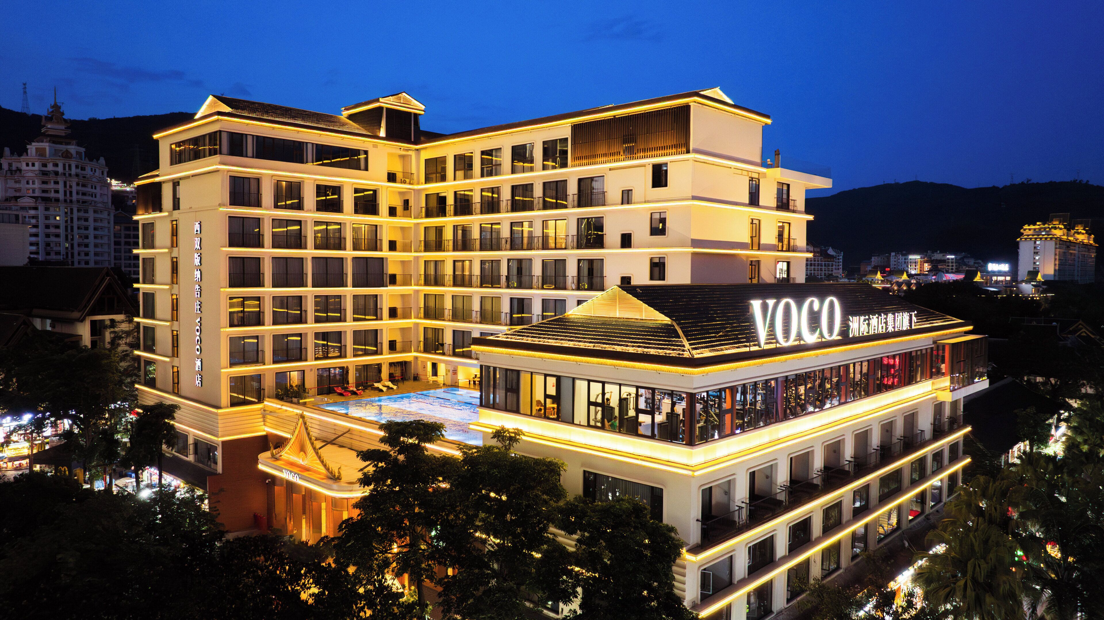 A multi-story hotel with a prominent 'Voco' sign, a rooftop pool, and a modern architectural design.