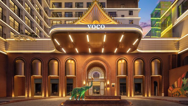 A hotel entrance with a prominent 'YOCO' sign, a central archway, and a dinosaur sculpture in the courtyard. - voco Xishuangbanna Gaozhuang by IHG (Xishuangbanna Dai)