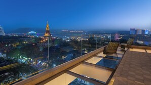 A rooftop terrace with glass flooring, two wicker chairs, and a view of a cityscape at dusk. - voco Xishuangbanna Gaozhuang by IHG (Xishuangbanna Dai)